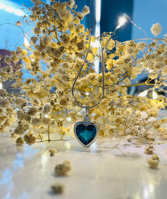 Heart-shaped blue pendant with a blurred background of white flowers and lights